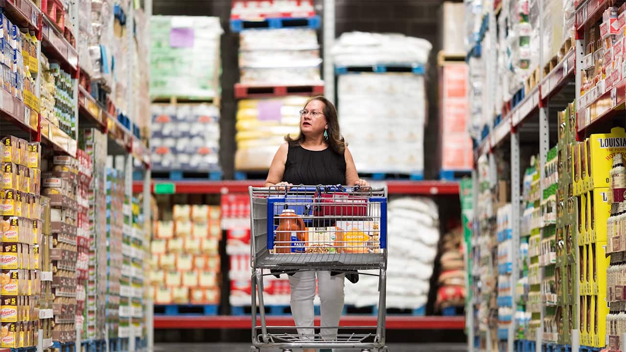 woman pushing shopping cart inside large warehouse member store