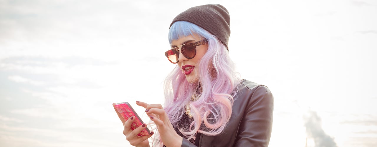 blue-pink hair cool girl wearing black leather jacket, beanie and sunglasses, texting on smart phone