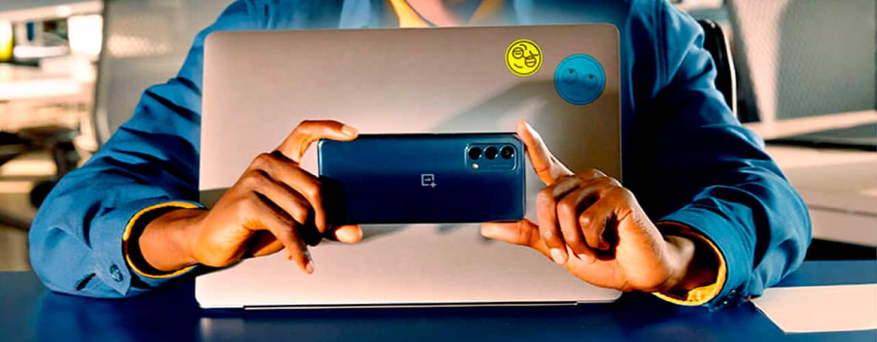 hands holding phone oneplus Nord N200 5G in front of laptop inbody