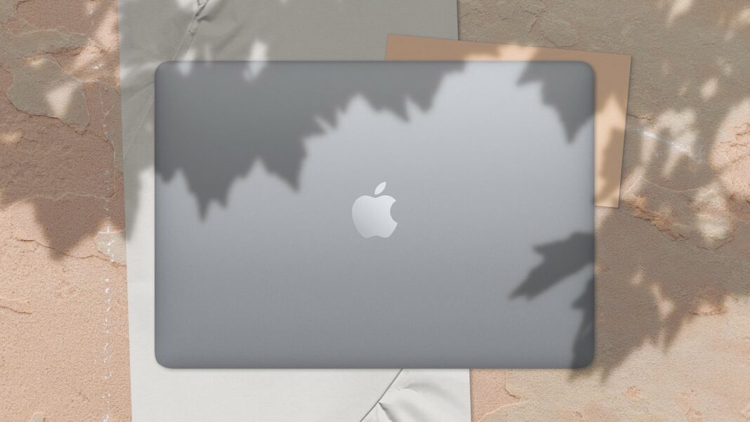 macbook air 13 inch space grey on tan wall with paper behind and leaves as shadow