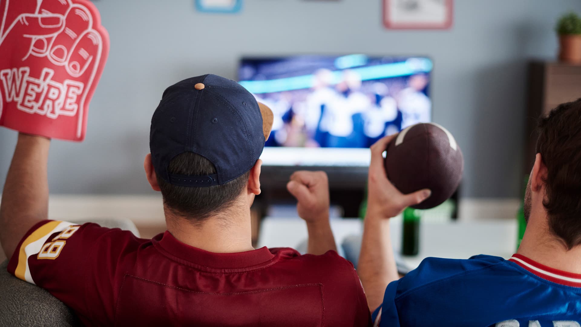 two men on couch excited watching football in jerseys