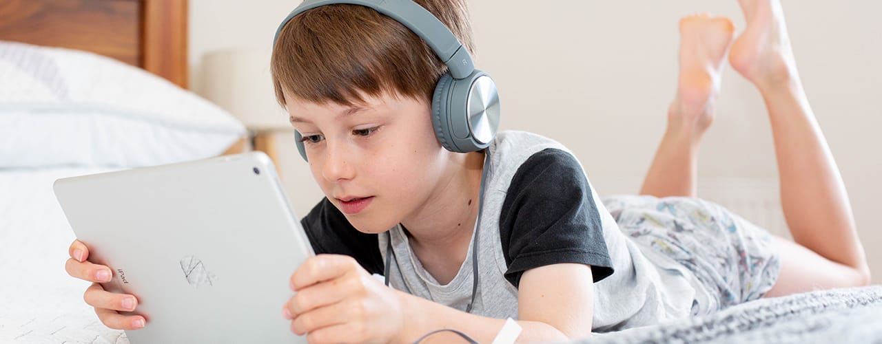 boy using ipad with headphones on bed