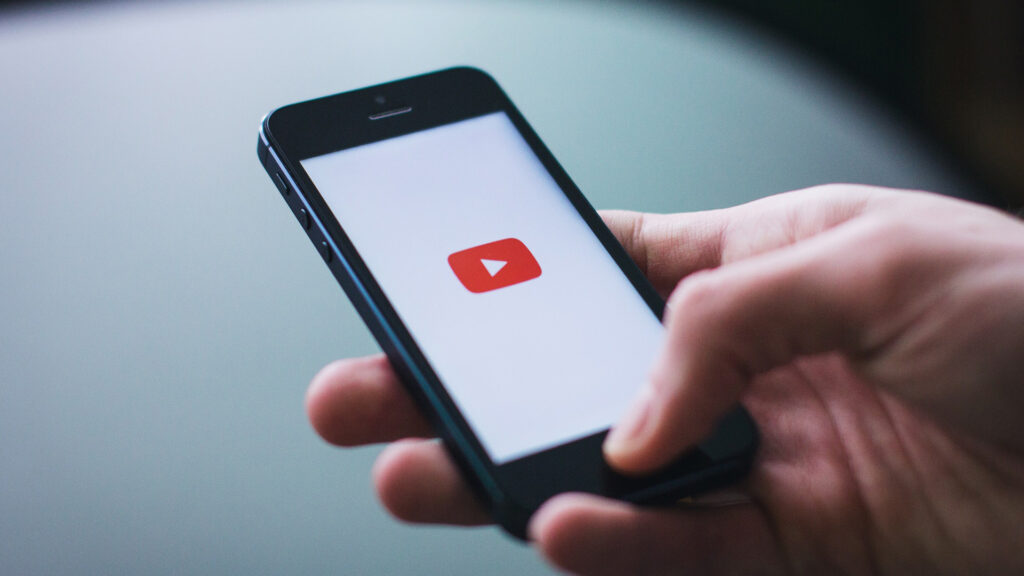 Mão segurando o smartphone com o botão de reprodução do YouTube