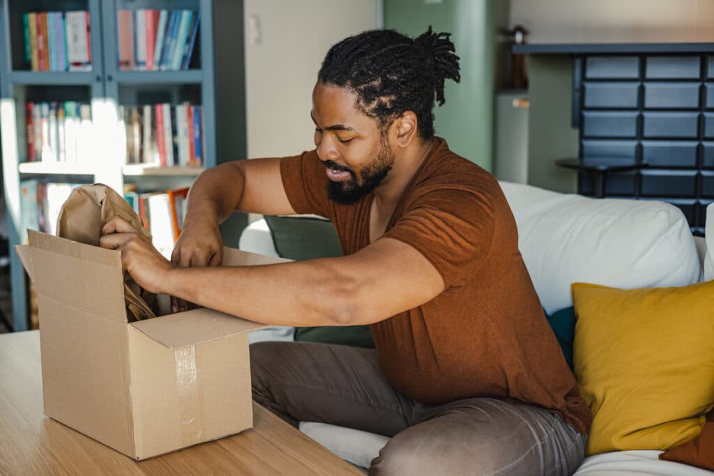 Man sitting on couch while opening shipping box