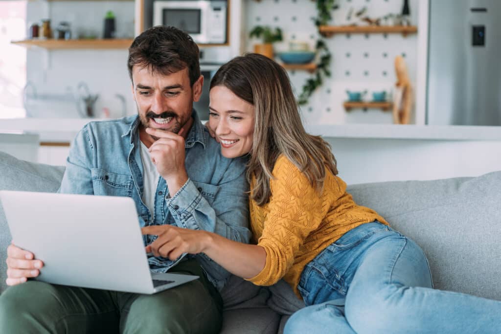 Man and woman smiling and looking at laptop while sitting on a couch