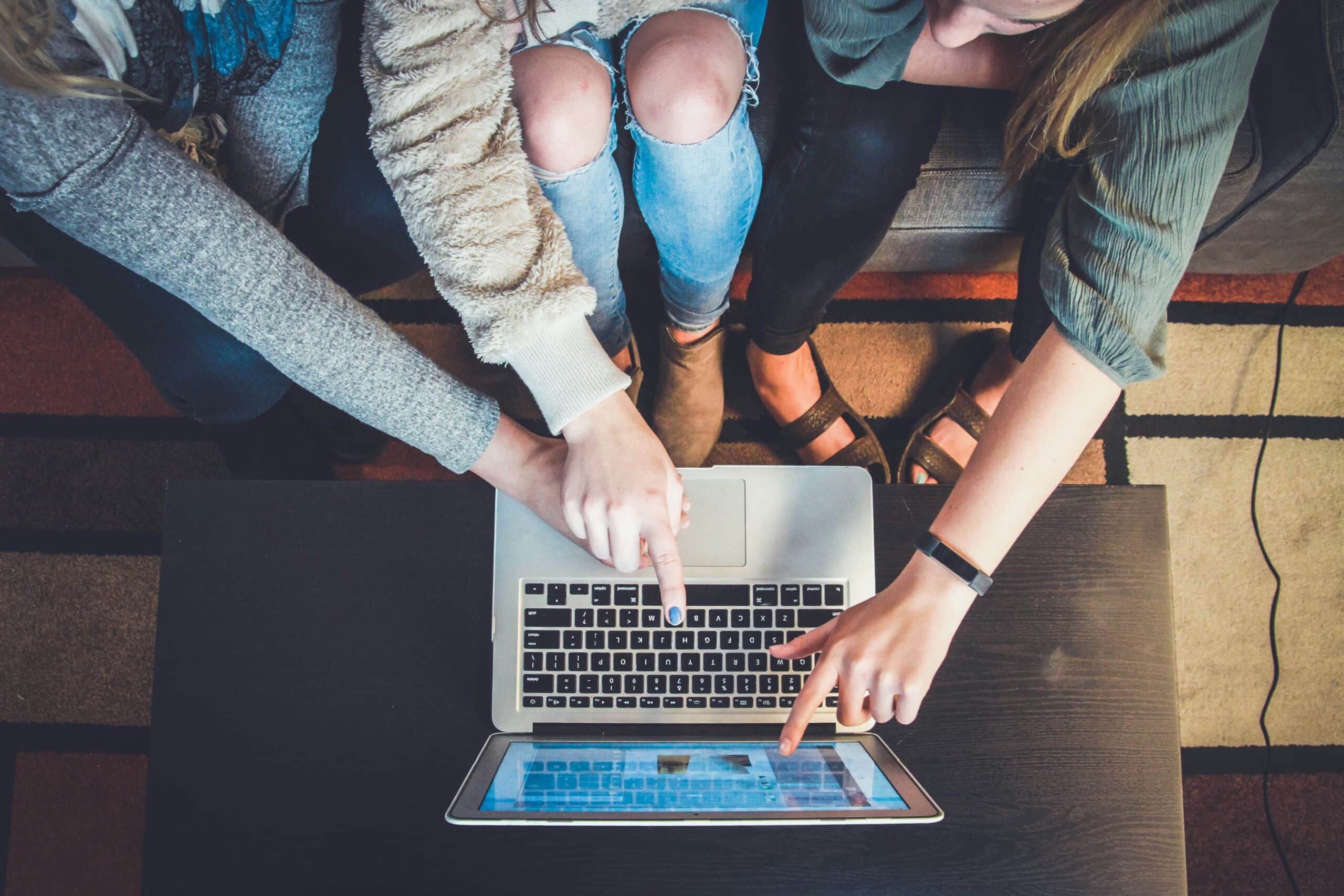 three people sitting around a laptop pointing at the screen.