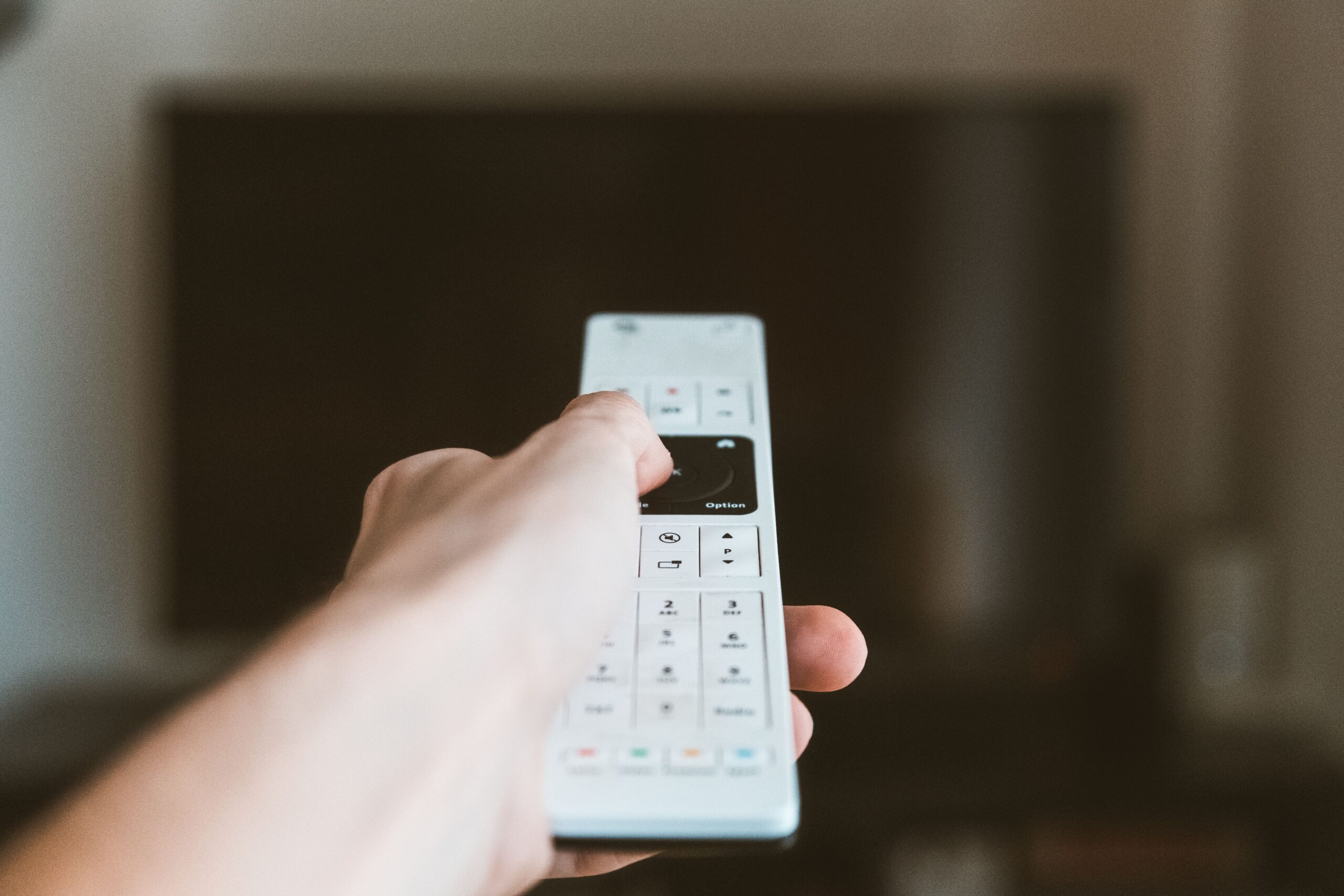 Hand holding a remote control with a TV in the background.