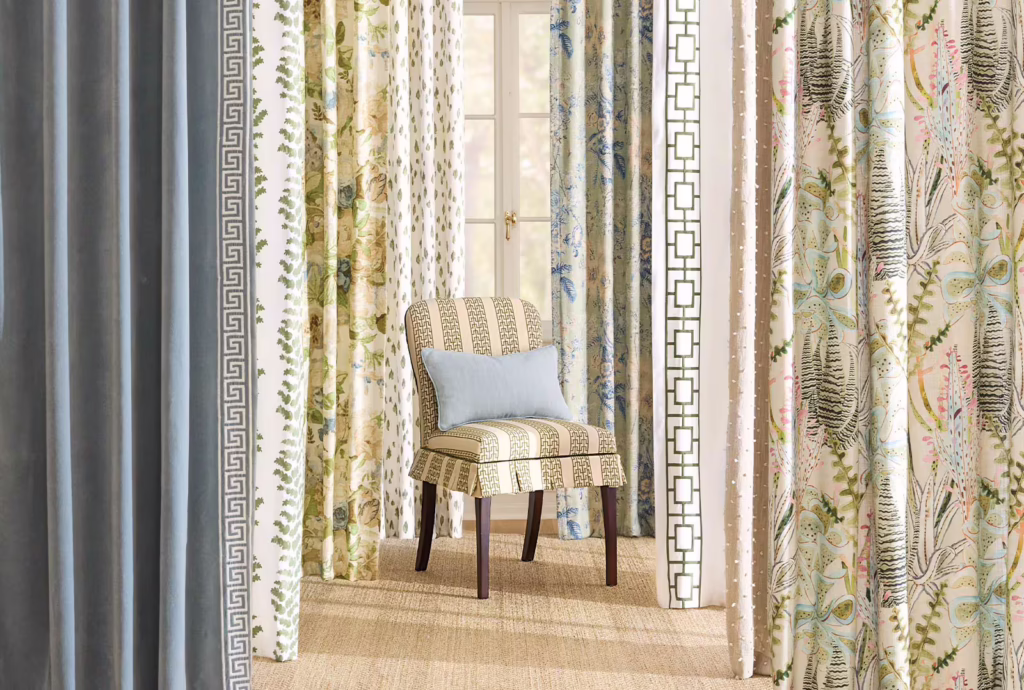 Ballard Designs drapery panels in assorted patterns and fabrics surrounding an upholstered accent chair with a light blue pillow.