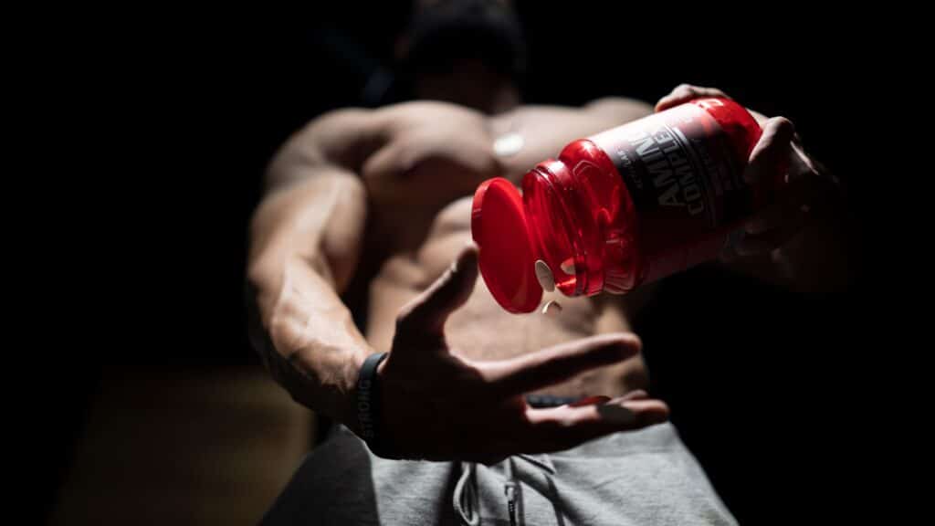 A man pouring supplement capsules from a red bottle into his hand.
